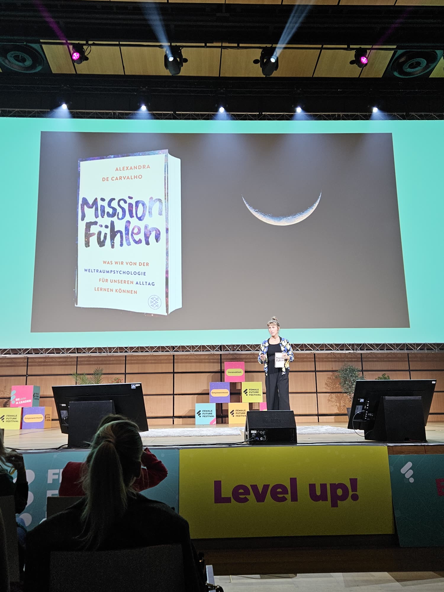 Alexandra de Carvalho auf der Bühne, hinter ihr das Buch Mission Fühlen und ein Mond